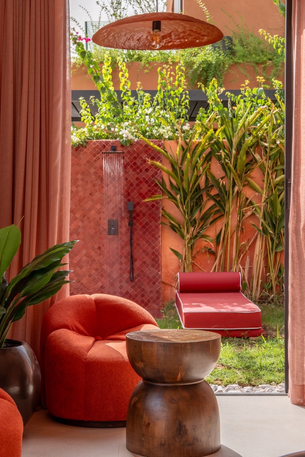 Suite avec fauteuil bouclé orange, douche extérieure en zellige et jardin tropical